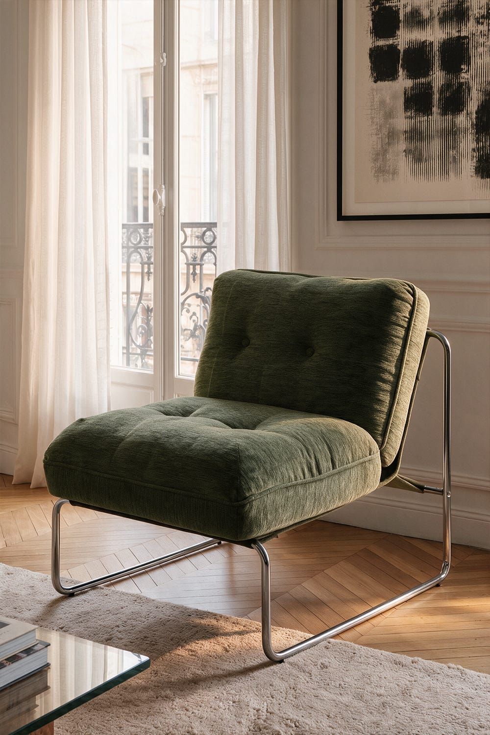 Sillón verde oscuro de estructura tubular junto a un ventanal con cortinas claras